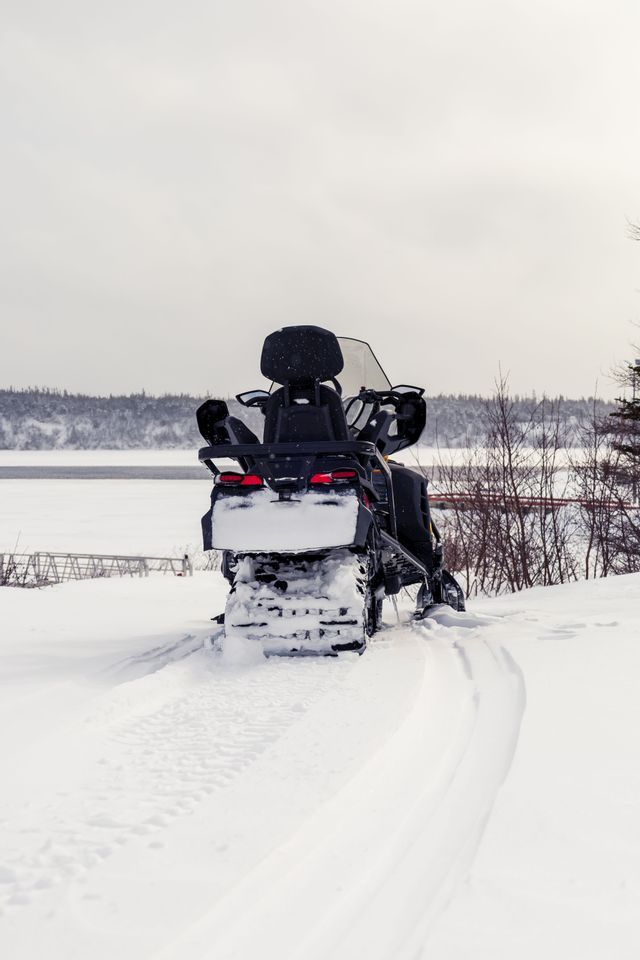 Una motoslitta nera è parcheggiata su un paesaggio innevato, con le sue tracce visibili in primo piano e un lago ghiacciato sullo sfondo.