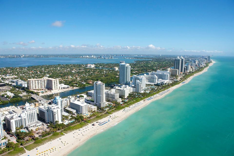 Vista aerea di una città costiera con grattacieli bianchi lungo una spiaggia sabbiosa e acqua oceanica turchese.