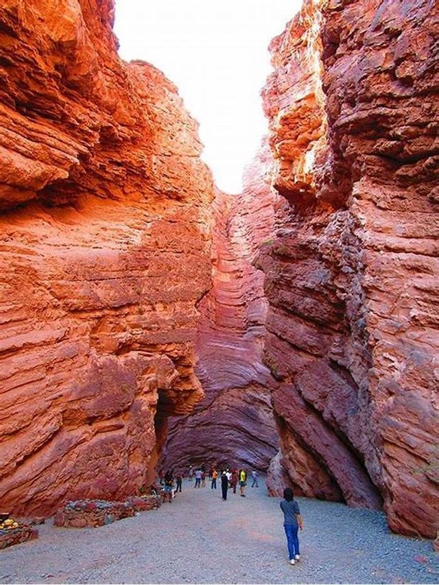 Un viaje en grupo de WeRoad camina por un estrecho pasaje de cañón con altas paredes de roca roja en capas.