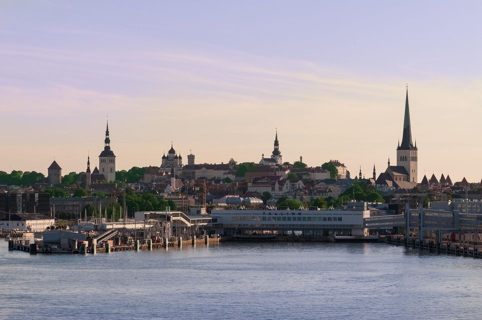Skyline storico cittadino con numerose guglie di chiese e torri medievali, visto dall'acqua con un porto moderno in primo piano.
