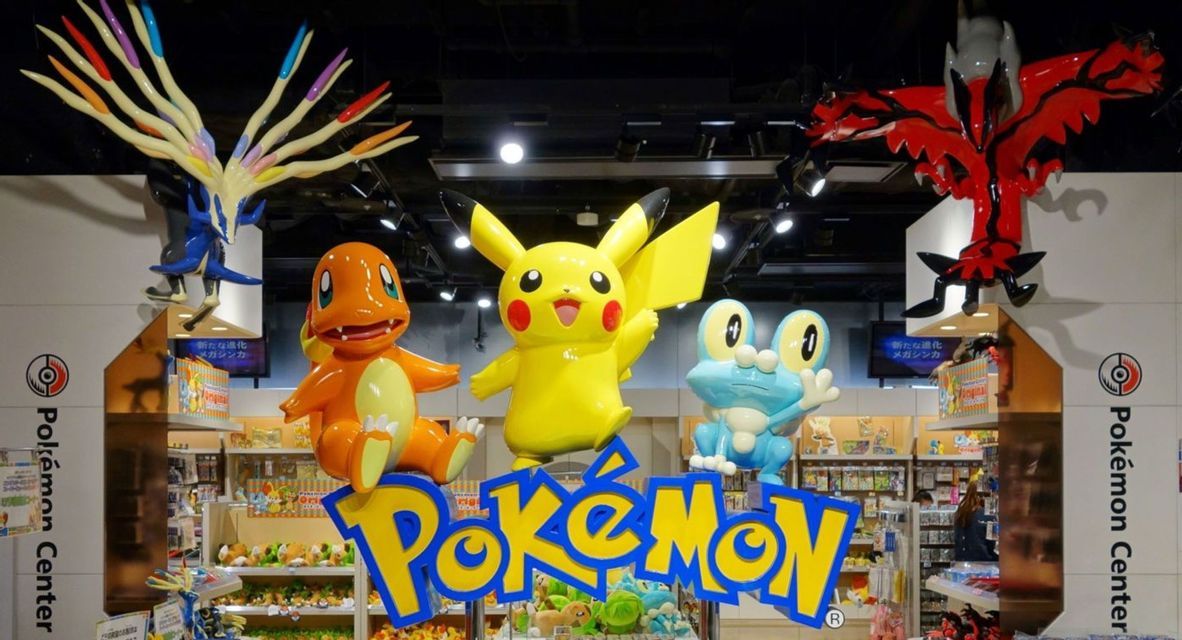 Grandi statue colorate dei personaggi Pokémon Pikachu, Charmander e Froakie all'interno di un negozio Pokémon Center.