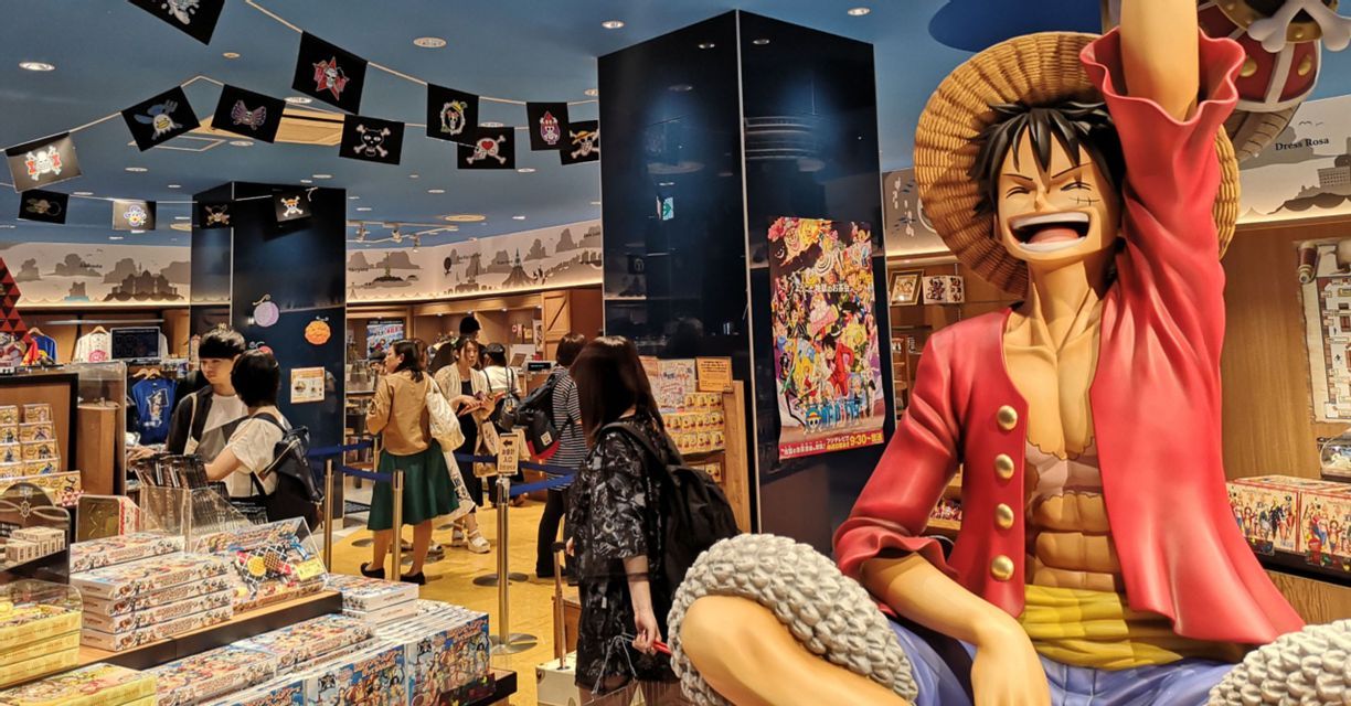 Una grande statua del personaggio anime Luffy di One Piece all'interno di un negozio di merchandising a tema con clienti che curiosano.