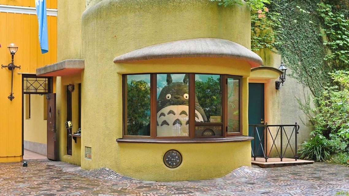 Una grande figura del personaggio di Totoro si trova all'interno della finestra di una biglietteria di un edificio giallo curvo e stravagante.