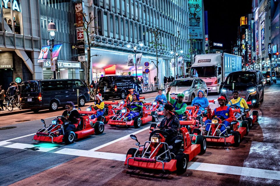 Un viaggio di gruppo WeRoad con persone in costumi colorati che guidano go-kart rossi su una strada cittadina di notte.