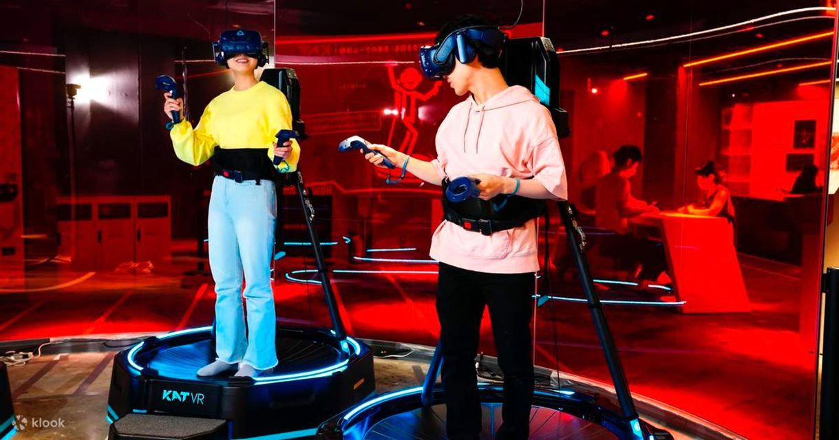 Due persone con visori per la realtà virtuale e imbracature giocano su piattaforme circolari in una stanza con luci al neon rosse e blu.