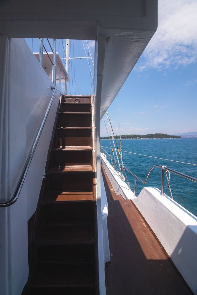 A view from the deck of a boat, showing wooden stairs leading up, with the blue sea and a distant island visible.