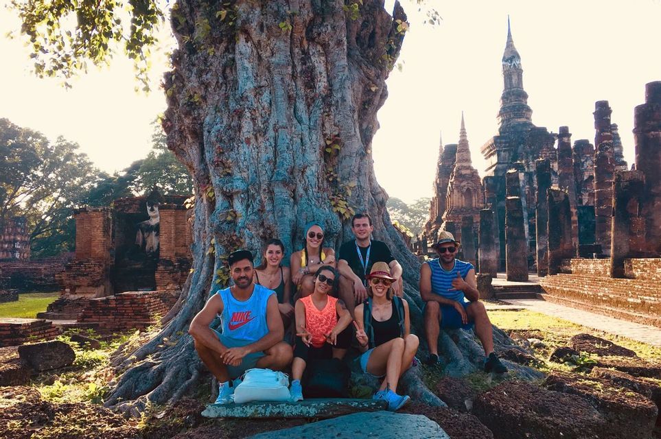 Un groupe WeRoad en voyage posant pour une photo au pied d'un grand arbre, avec des ruines de temples anciens et une statue de Bouddha en arrière-plan.