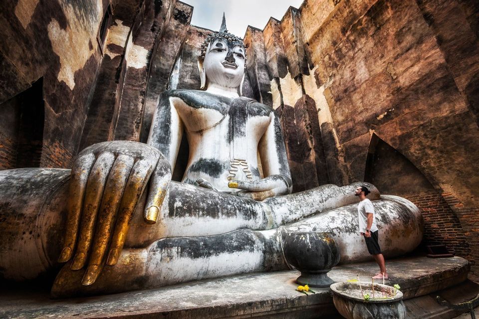Un homme contemple une gigantesque statue de Bouddha en pierre patinée, encadrée par d'imposants murs de briques.