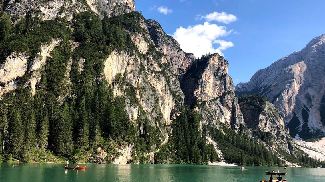 Eine WeRoad Gruppenreise mit Kanus auf einem türkisfarbenen See am Fuße großer, bewaldeter Berge unter blauem Himmel.