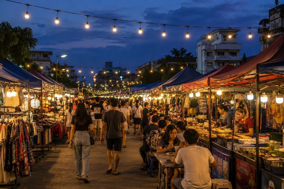 Un vivace mercato di strada di notte, con persone che fanno acquisti e mangiano alle bancarelle sotto file di luci.