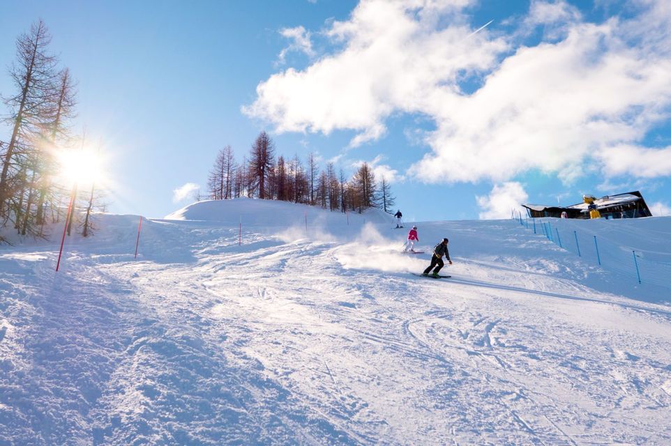 Eine WeRoad Gruppenreise zum Skifahren und Snowboarden auf einem verschneiten Berghang an einem sonnigen Tag bei strahlend blauem Himmel.