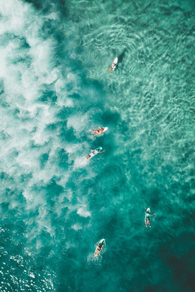 Luftaufnahme einer WeRoad Gruppenreise mit Personen auf Surfbrettern, die im klaren, türkisfarbenen Meerwasser schwimmen.