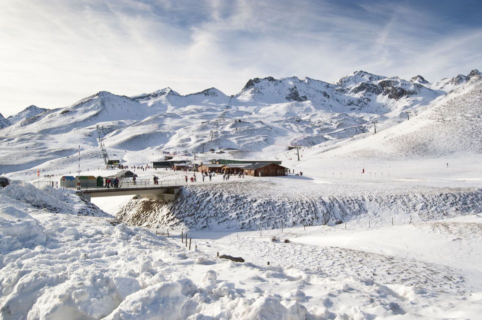 Una vista panorámica de una estación de esquí en una vasta cordillera cubierta de nieve bajo un cielo parcialmente nublado.