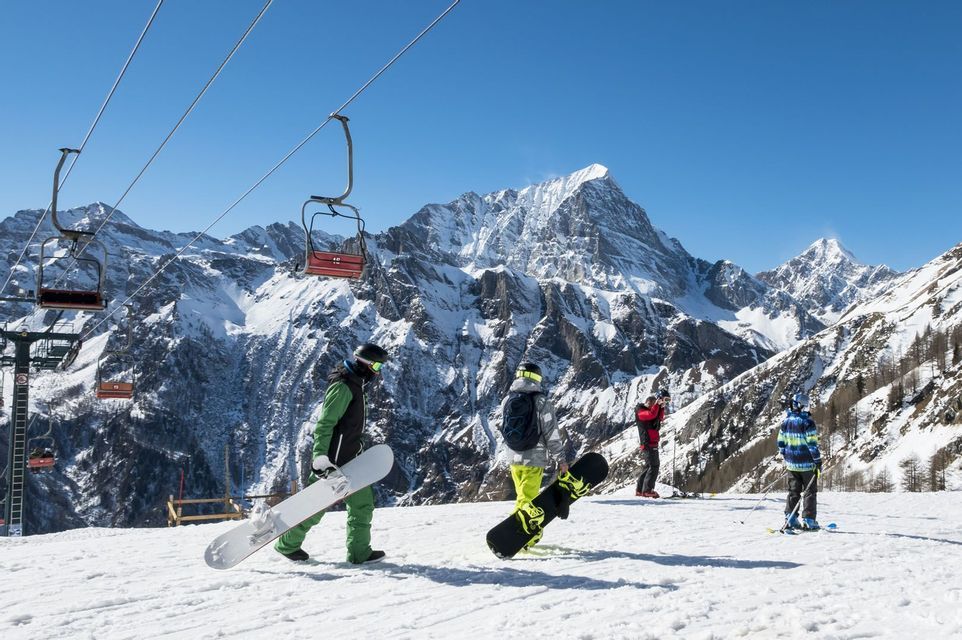 Viaje en grupo WeRoad con snowboarders en una pista nevada, con telesilla y montañas de fondo.