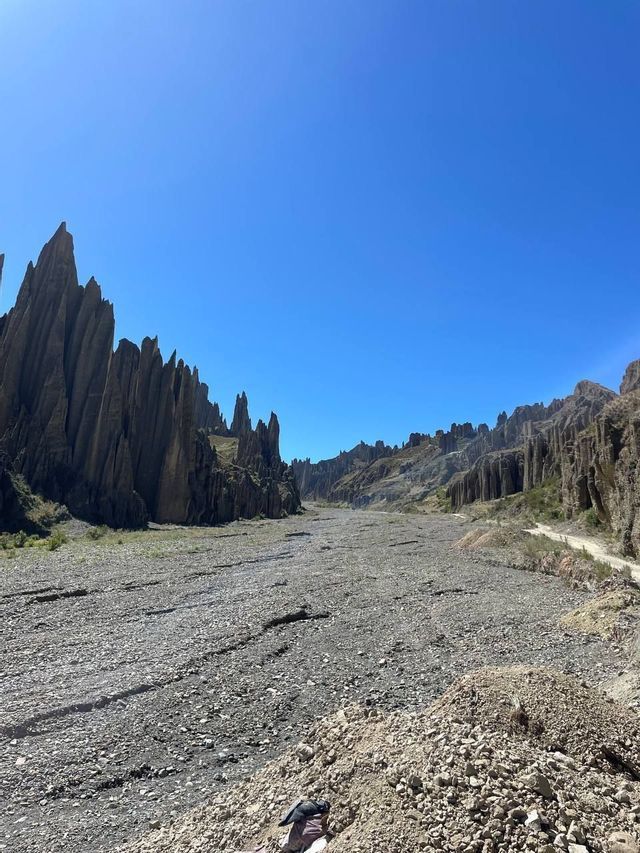 A wide, rocky canyon floor flanked by tall, spiky rock formations under a clear blue sky.