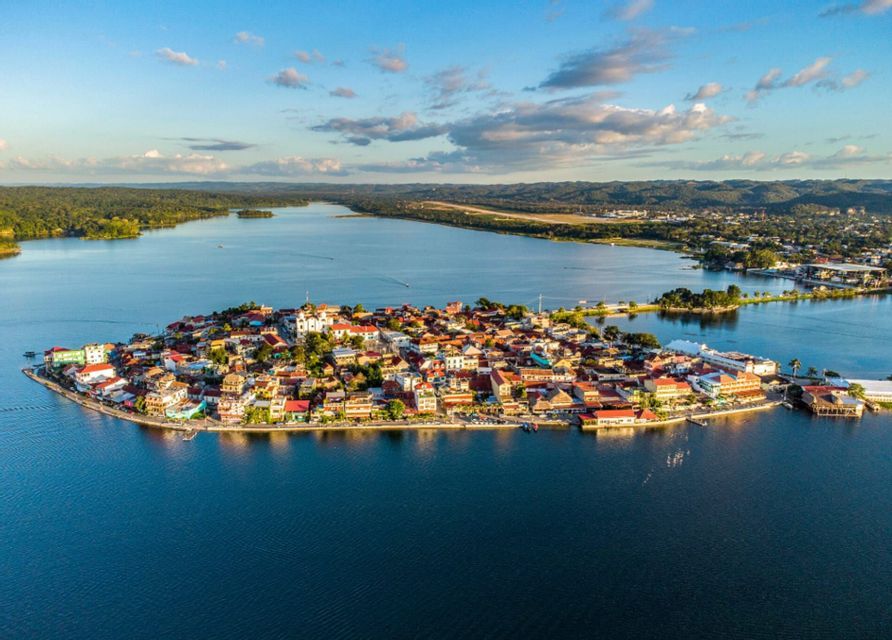 Eine Luftaufnahme einer kleinen, dicht besiedelten Inselstadt an einem blauen See, mit einem bewaldeten Festland im Hintergrund.