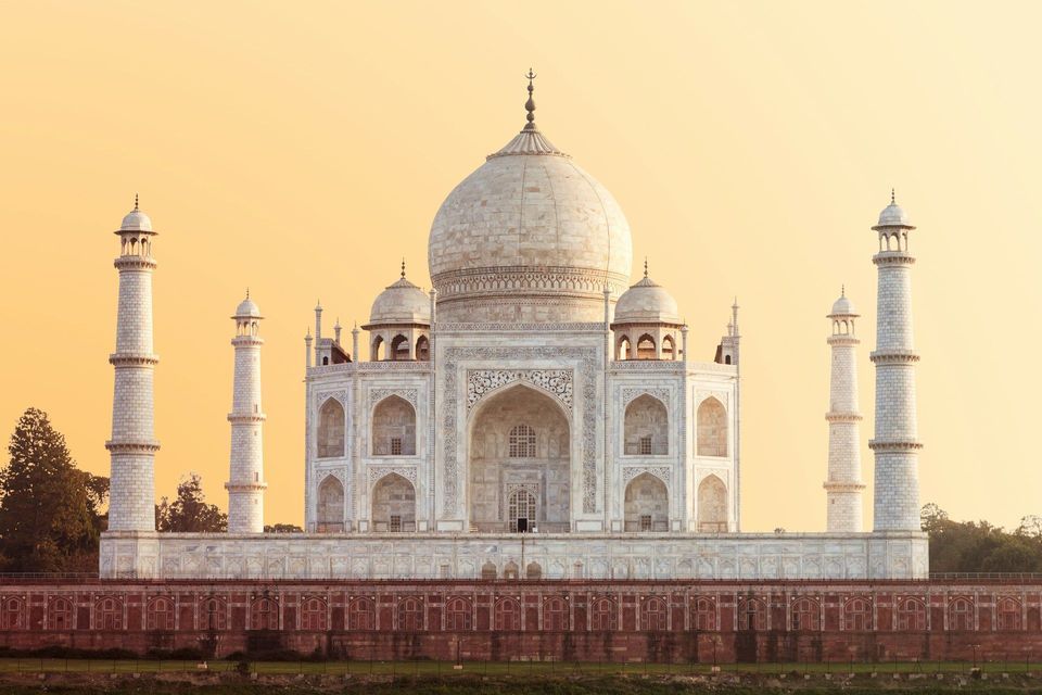 Un mausoleo di marmo bianco con una grande cupola centrale e quattro minareti è illuminato da un cielo caldo e dorato all'alba.