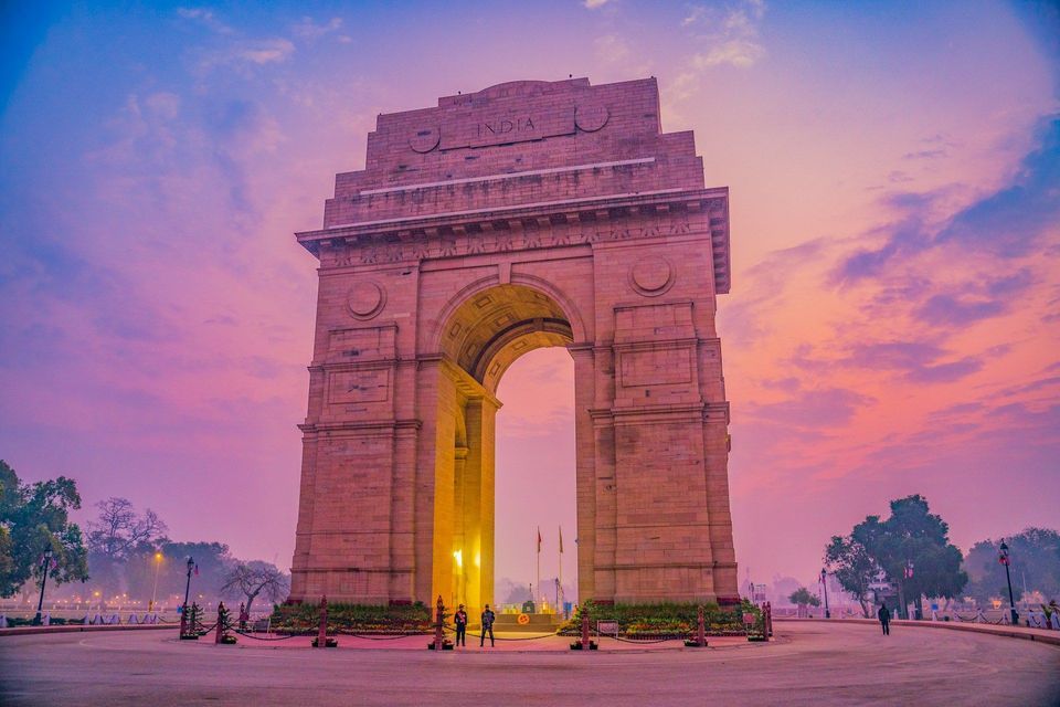 Il monumento India Gate illuminato all'alba, che si staglia su un cielo con nuvole rosa e blu.