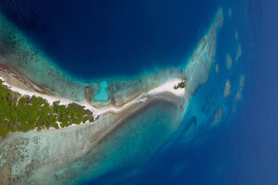 Veduta aerea di un'isola tropicale, con il suo banco di sabbia bianca e la barriera corallina che contrastano con il mare turchese e blu profondo.