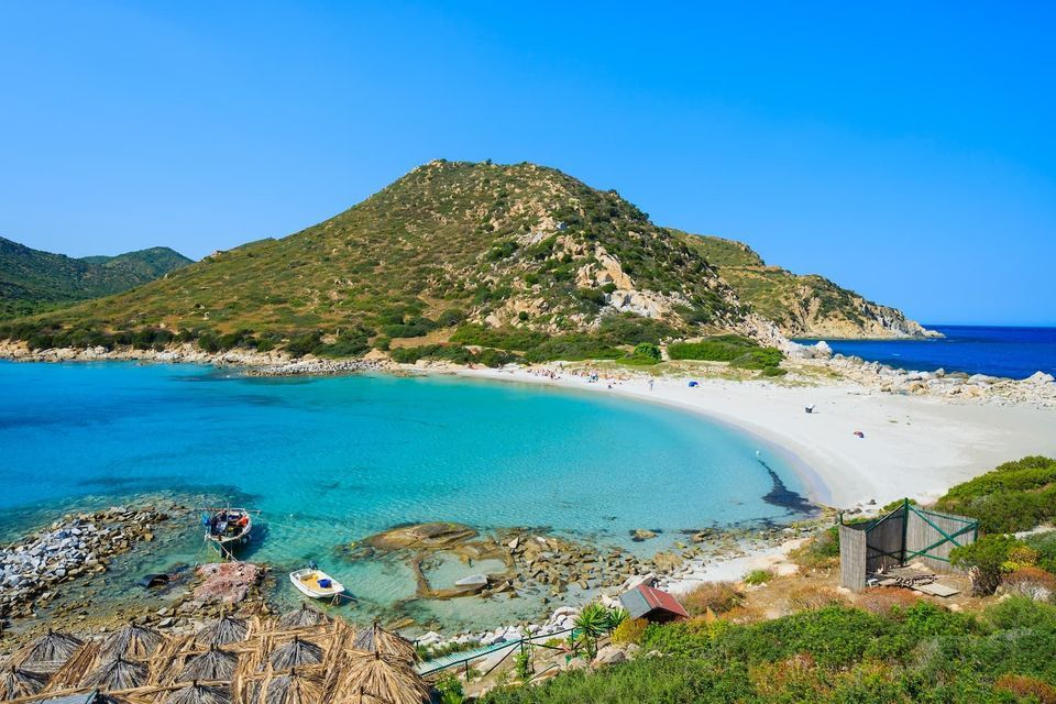 Una vista dall'alto di una caletta appartata con una spiaggia di sabbia bianca e acqua turchese, incastonata contro una grande collina verde.