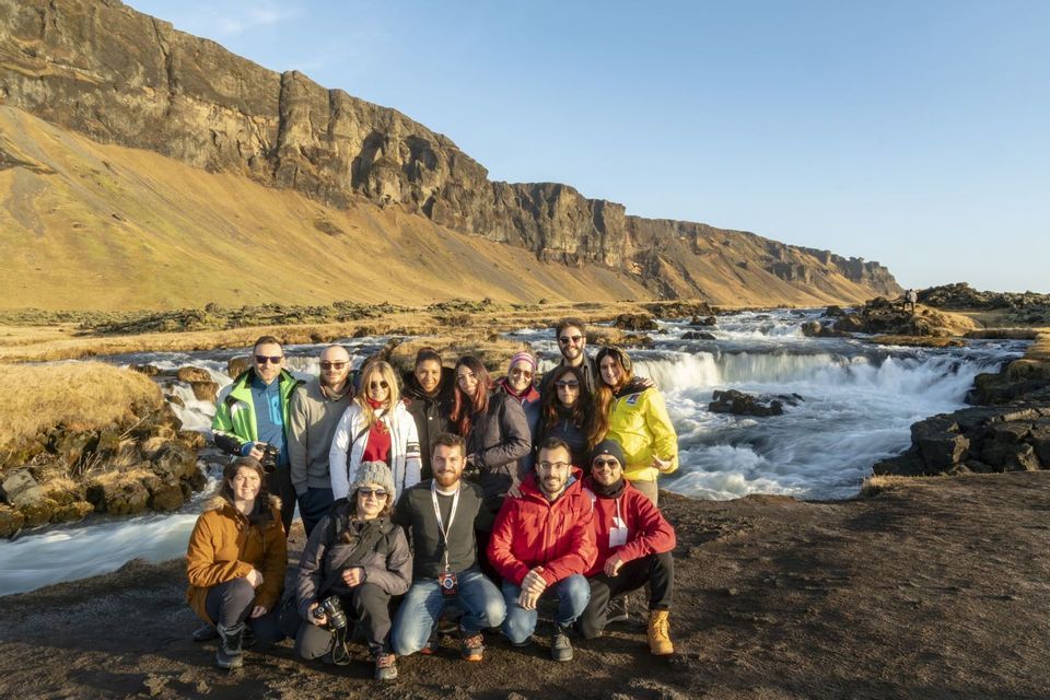 Un viaje en grupo de WeRoad posa para una foto frente a un río caudaloso en la base de un acantilado rocoso e iluminado por el sol.
