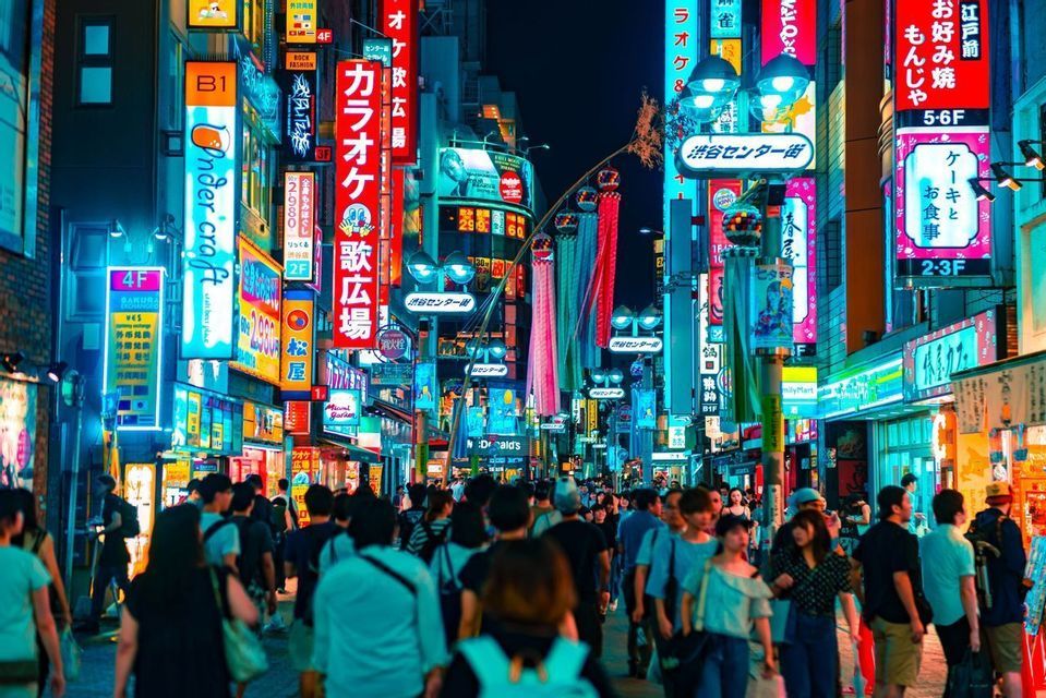 A crowd of people walking down a busy city street at night, illuminated by the glow of colorful neon signs.