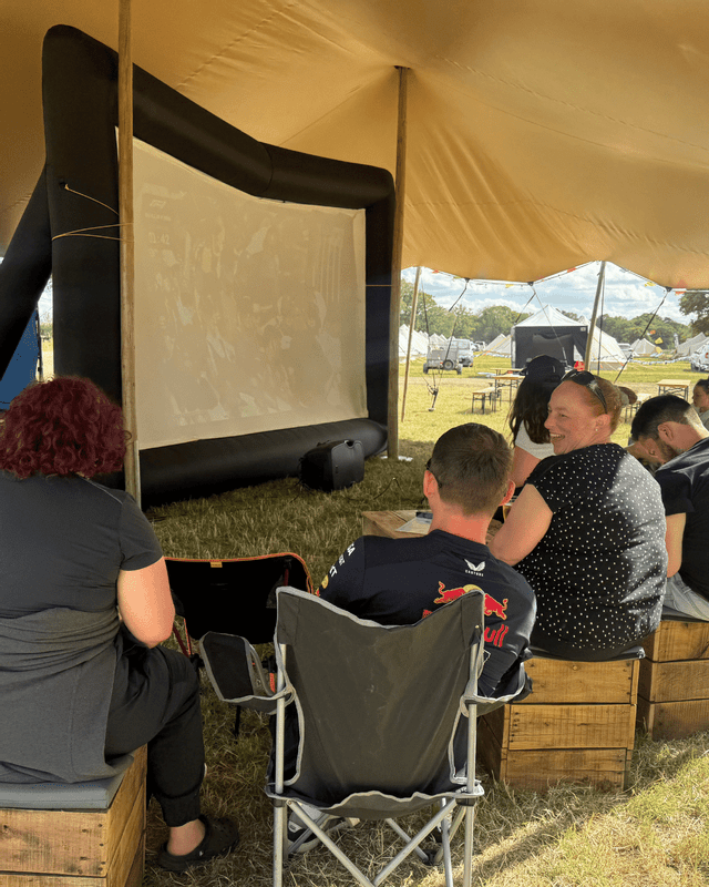 A WeRoad group trip sits under a large tent, watching an inflatable movie screen during an outdoor event.