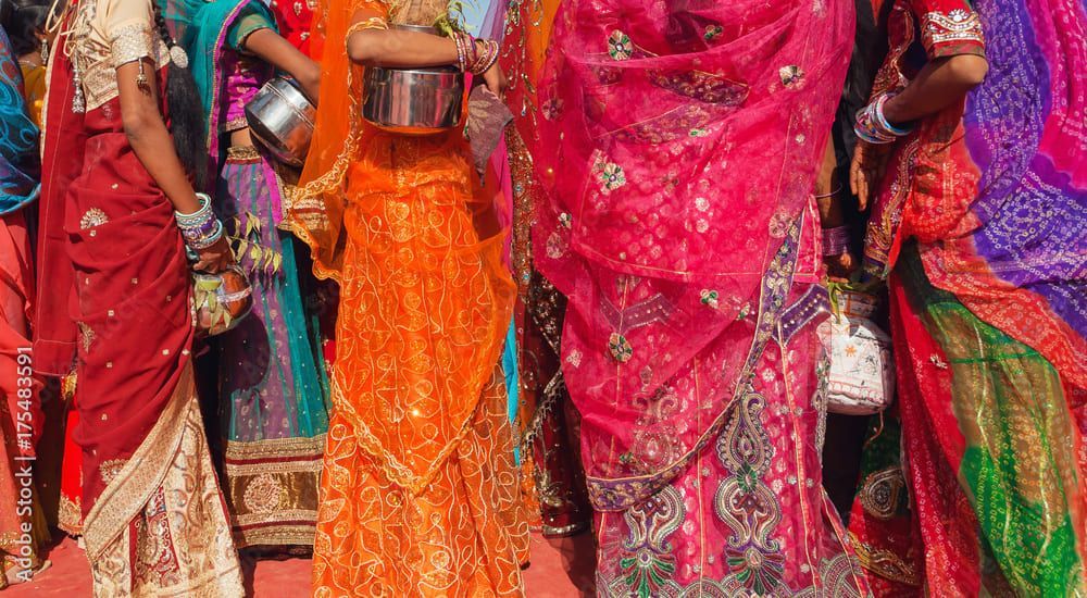 Un grupo de mujeres de pie, muy unidas, luciendo vibrantes y coloridos saris indios tradicionales y sosteniendo pequeñas vasijas.