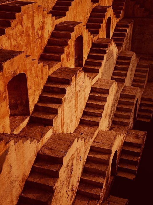 Una rete intricata di scalinate in pietra intrecciate scende con un motivo geometrico all'interno di un antico pozzo a gradini.
