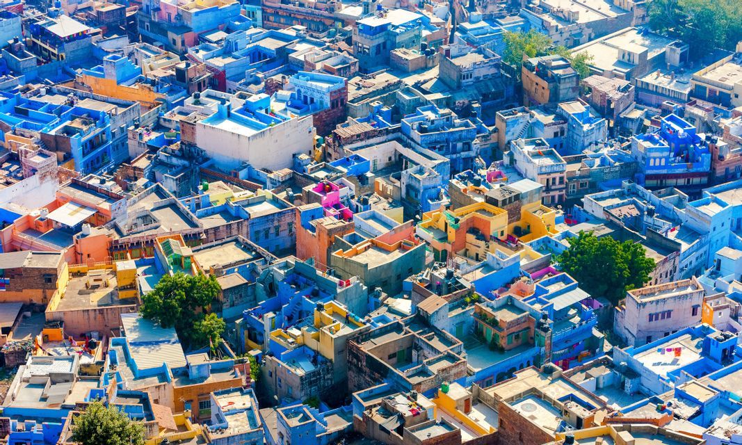 Una vista aerea di una città densa, con molti edifici dai tetti piatti dipinti in tonalità di blu, giallo e rosa.