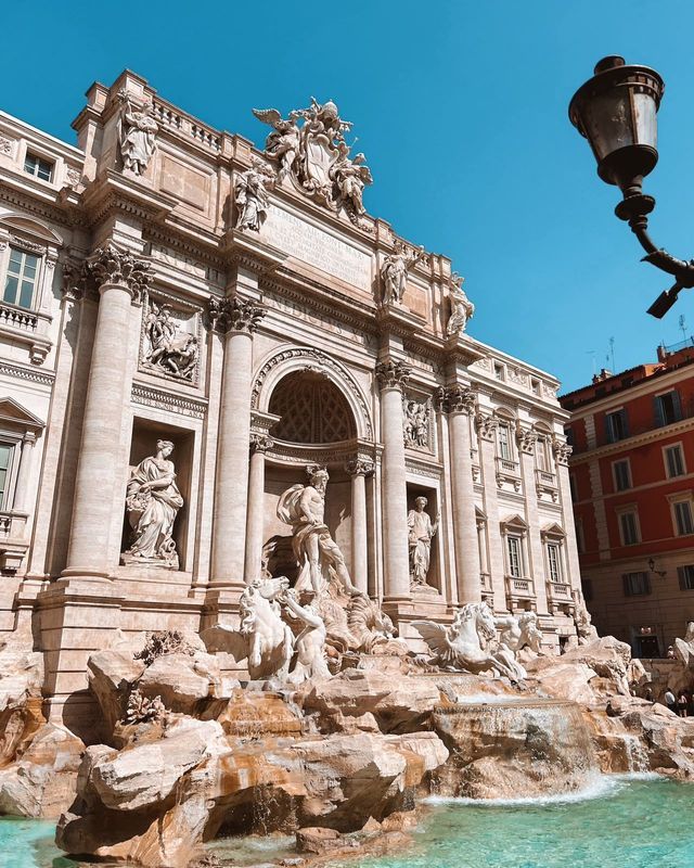 A low-angle daytime view of a large, ornate fountain with intricate statues built against a classical building.