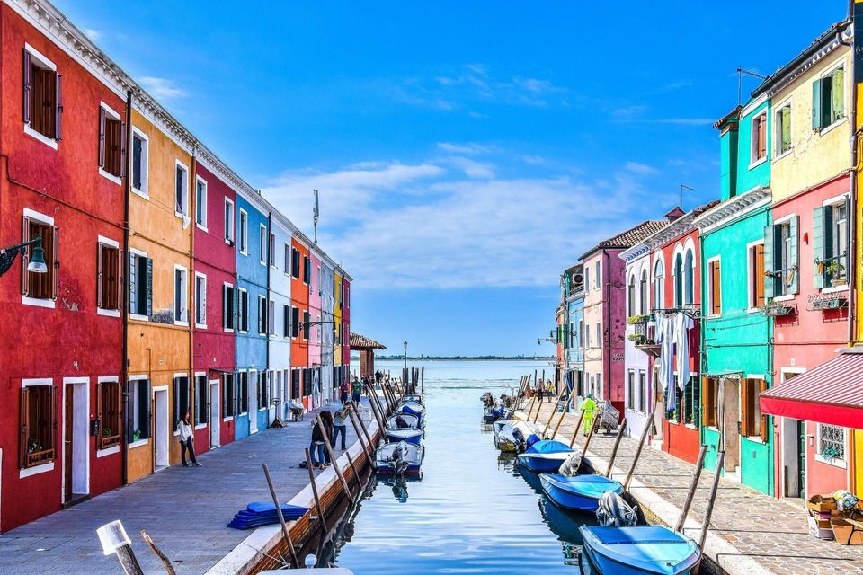 Brightly colored houses line a narrow canal filled with docked boats under a clear blue sky.