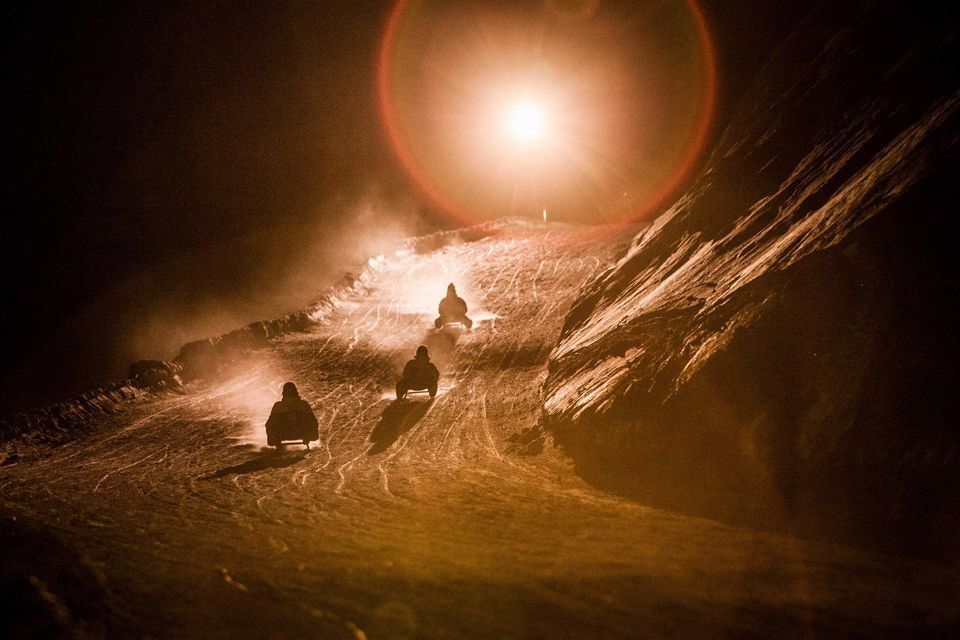 Un viaggio di gruppo WeRoad in slitta lungo un pendio innevato di notte, illuminato da una brillante luce dall'alto.