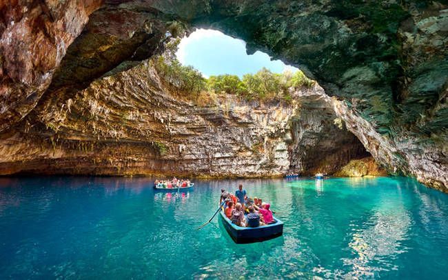 Un viaggio di gruppo WeRoad esplora una grande grotta marina con acque turchesi a bordo di piccole imbarcazioni, illuminate da un'apertura soleggiata dall'alto.