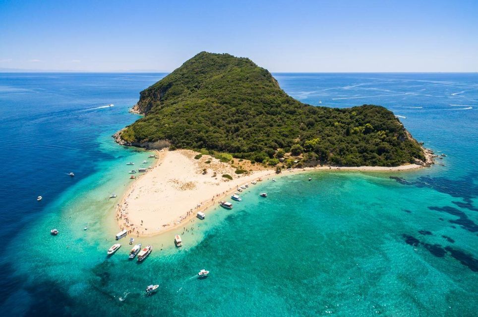 Vista aerea di un'isola alberata con una lingua di sabbia dove le barche sono ormeggiate e le persone si godono l'acqua turchese.