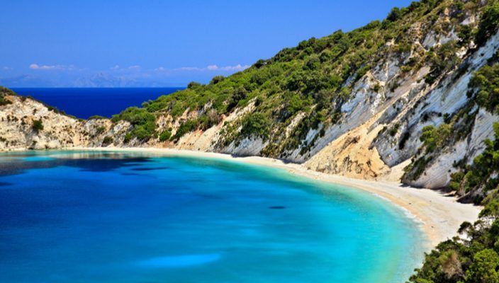 Una caletta appartata con acqua turchese cristallina e una spiaggia di sabbia bianca, incastonata tra verdi scogliere alberate sotto un cielo azzurro.