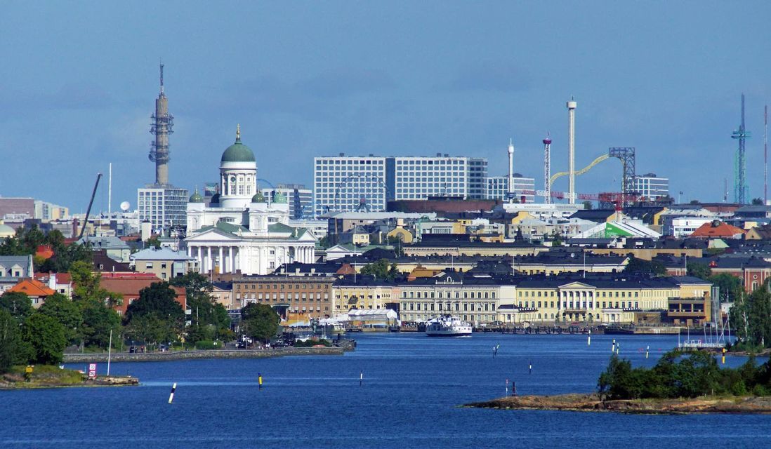 Un paysage urbain vu de la mer, avec une cathédrale blanche au dôme vert, un ferry sur l'eau et un parc d'attractions en arrière-plan.