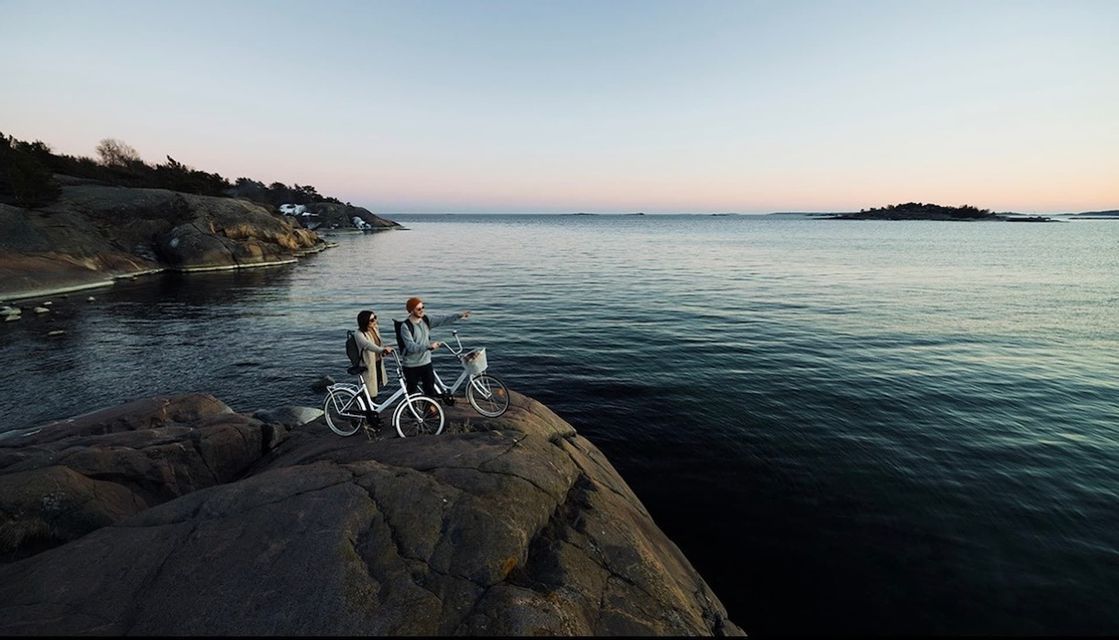 Deux personnes d'un voyage en groupe WeRoad avec leurs vélos sur une falaise rocheuse, admirant la mer au coucher du soleil.