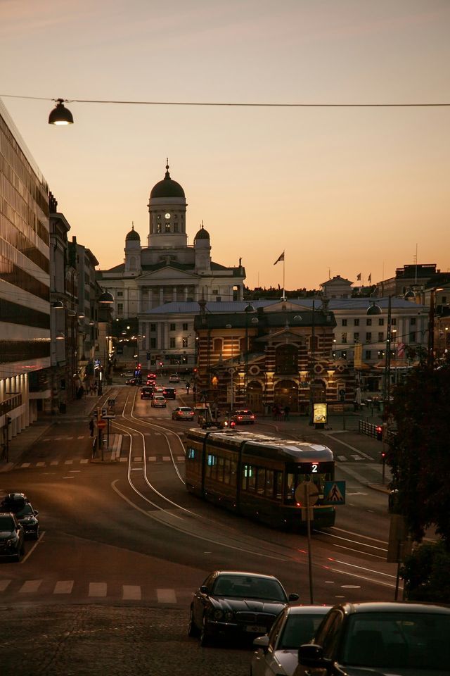 Un tramway circule sur les rails d'une rue urbaine au coucher du soleil, avec une grande cathédrale à dôme visible au loin.