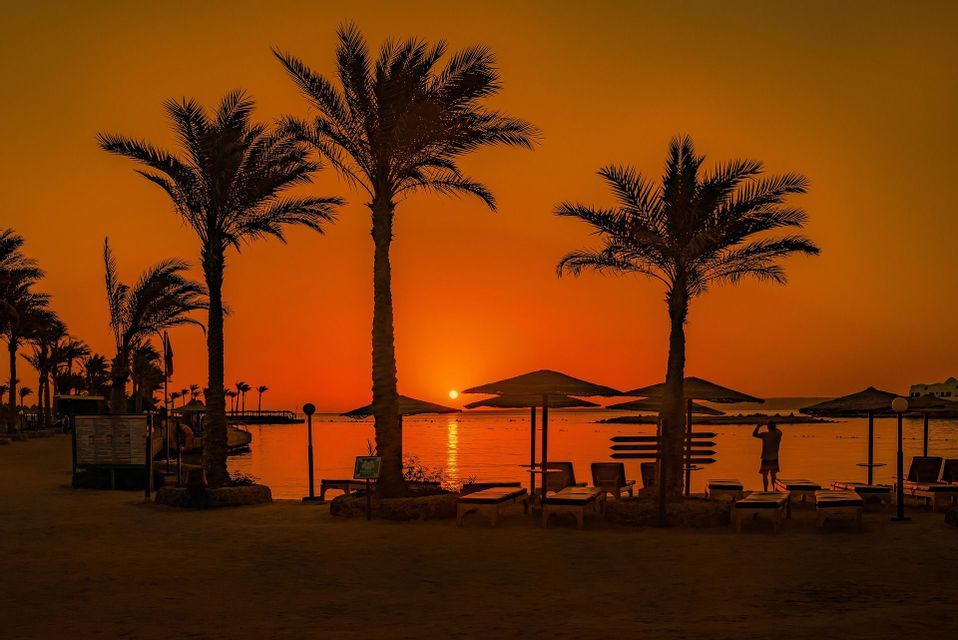 Palmen, Sonnenschirme und Sonnenliegen vor dem Hintergrund eines Sonnenuntergangs am Meer