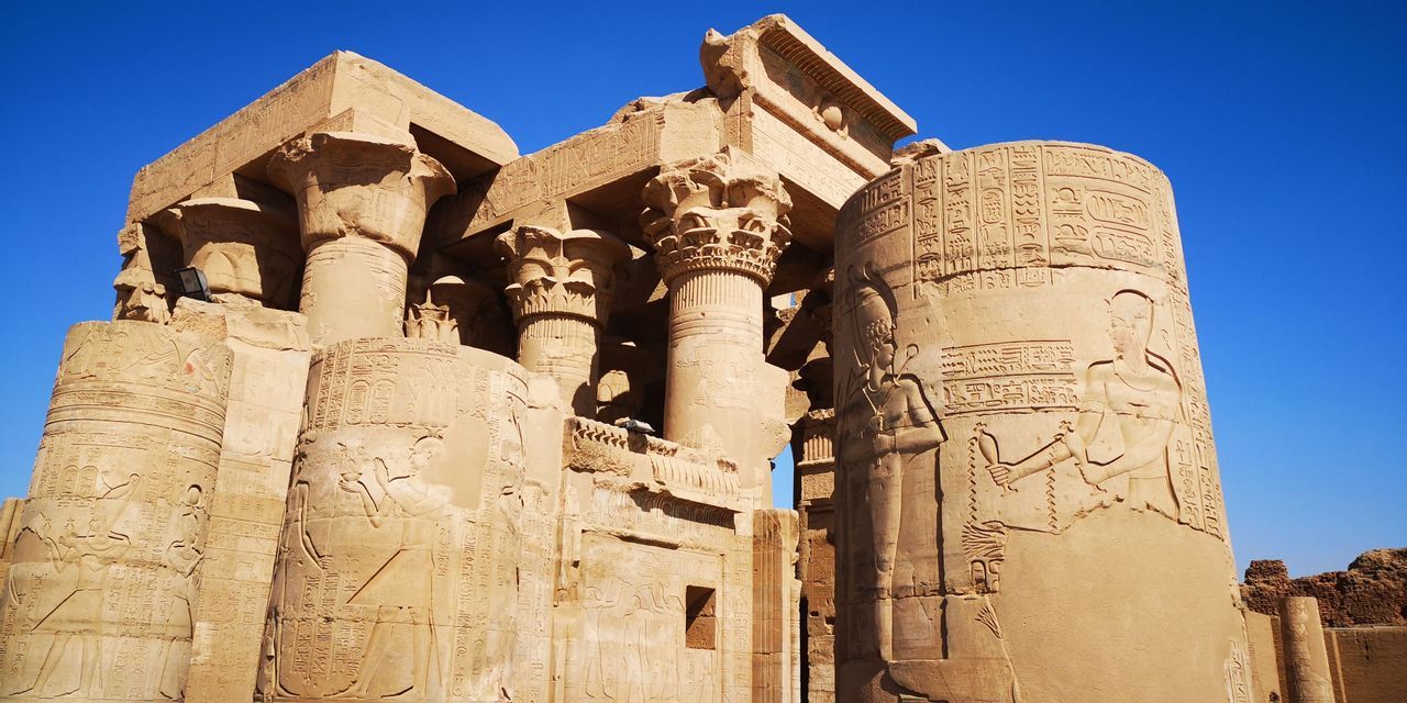 Alte Sandsteintempelruinen mit Säulen und hieroglyphischen Schnitzereien unter einem leuchtend blauen Himmel.