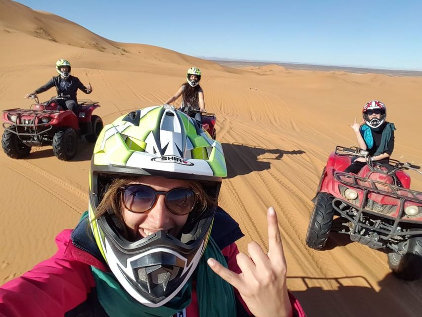Un grupo de WeRoad se hace un selfie mientras monta en quads rojos por extensas dunas de arena bajo un cielo azul claro.