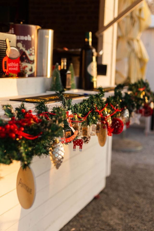 A close-up of a Christmas garland with small ornaments hanging from the front of a white wooden counter at an outdoor stall.