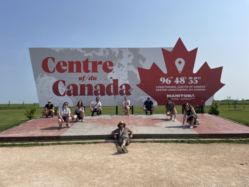Un viaggio di gruppo WeRoad in posa per una foto davanti al grande cartello 'Centre of Canada' in Manitoba.