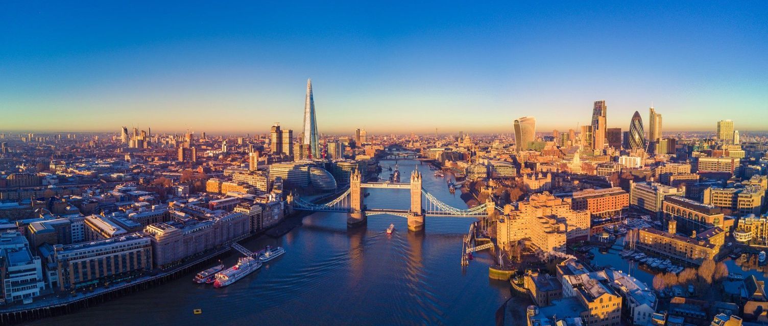 Una vista panoramica aerea di un fiume che attraversa una città densa con un ponte sospeso e grattacieli al tramonto.