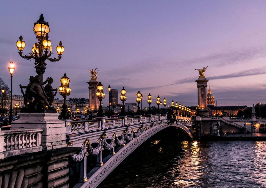 Un ponte di pietra decorato con lampioni d'epoca luminosi e sculture dorate che attraversa un fiume al crepuscolo