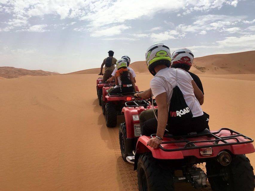 Un viaje en grupo WeRoad, montando quads rojos en fila por vastas dunas de arena del desierto bajo un cielo parcialmente nublado.