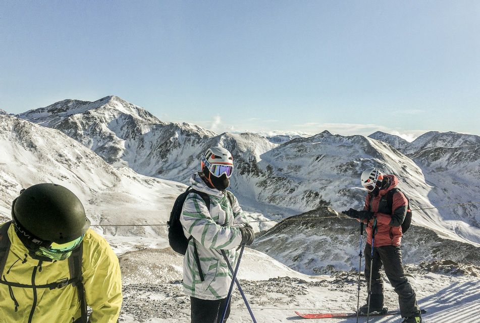 Un viaje en grupo de WeRoad de esquiadores con casco y gafas en la cima de una montaña nevada en un día despejado.