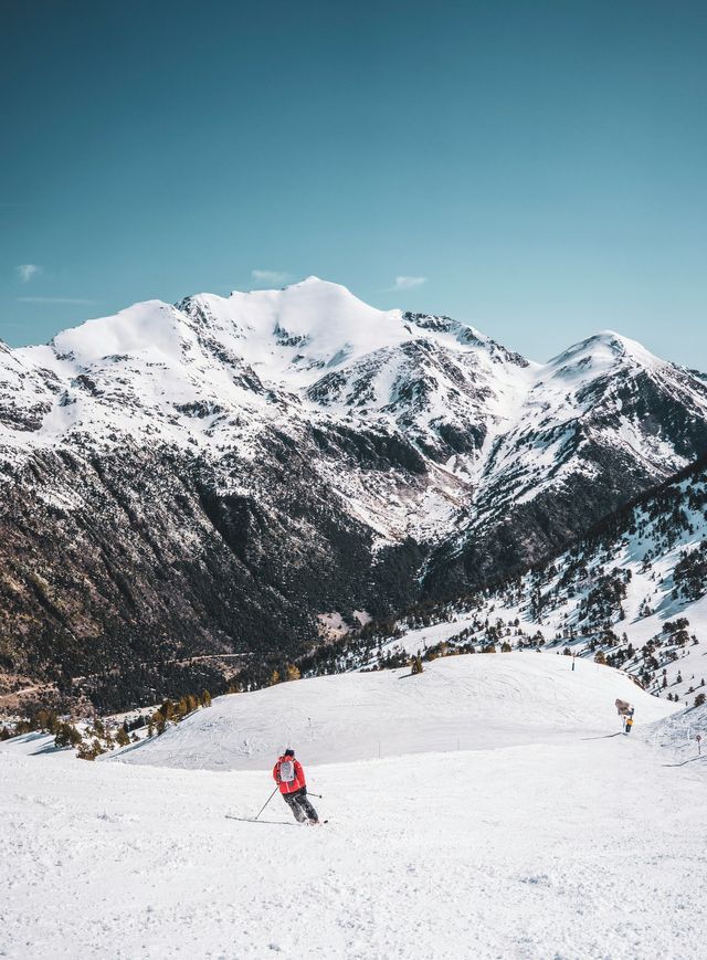 Un esquiador con chaqueta roja se desliza por una pendiente nevada con un fondo de montañas agrestes y cubiertas de nieve.