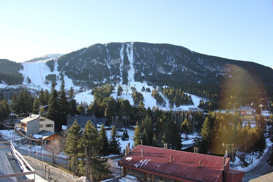 Las pistas de esquí cubiertas de nieve y los telesillas cruzan una montaña boscosa que se eleva sobre un pueblo con tejados de chalets.